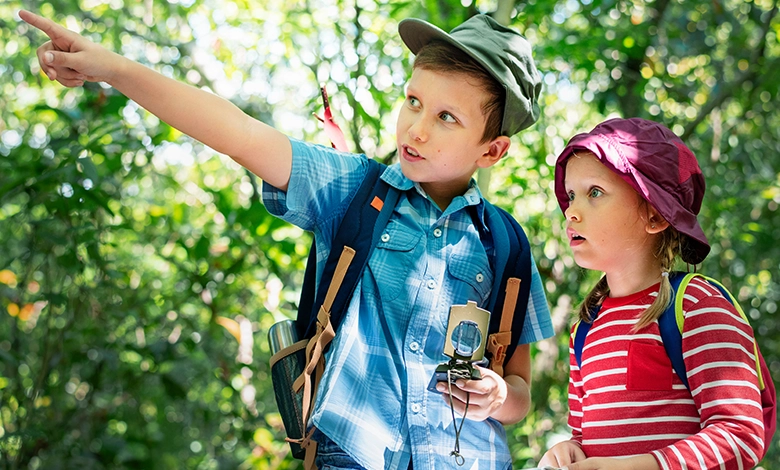 Young boy and girl exploring nature with compass and backpacks.
