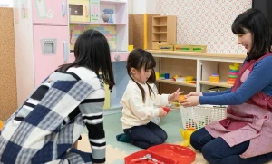 Two women and a child playing with toy kitchenware in a daycare.