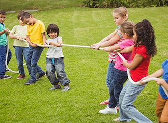 Group of children playing tug-of-war on a grassy field.