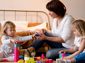 Woman playing with two children and colorful blocks indoors.