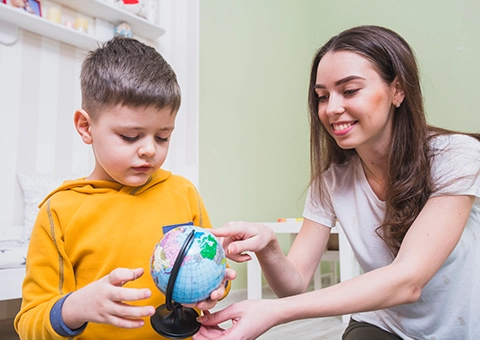 Child in yellow hoodie holding a small globe, adult assisting beside.