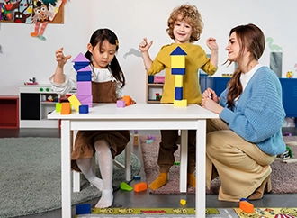 Children and teacher building with colorful blocks at a small table.