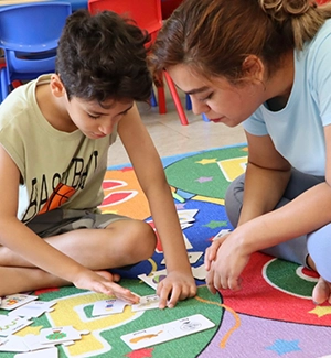 Child and teacher engaging in educational activity on a colorful rug.