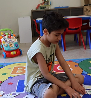 Child sitting on colorful alphabet rug, playing with cards in classroom.